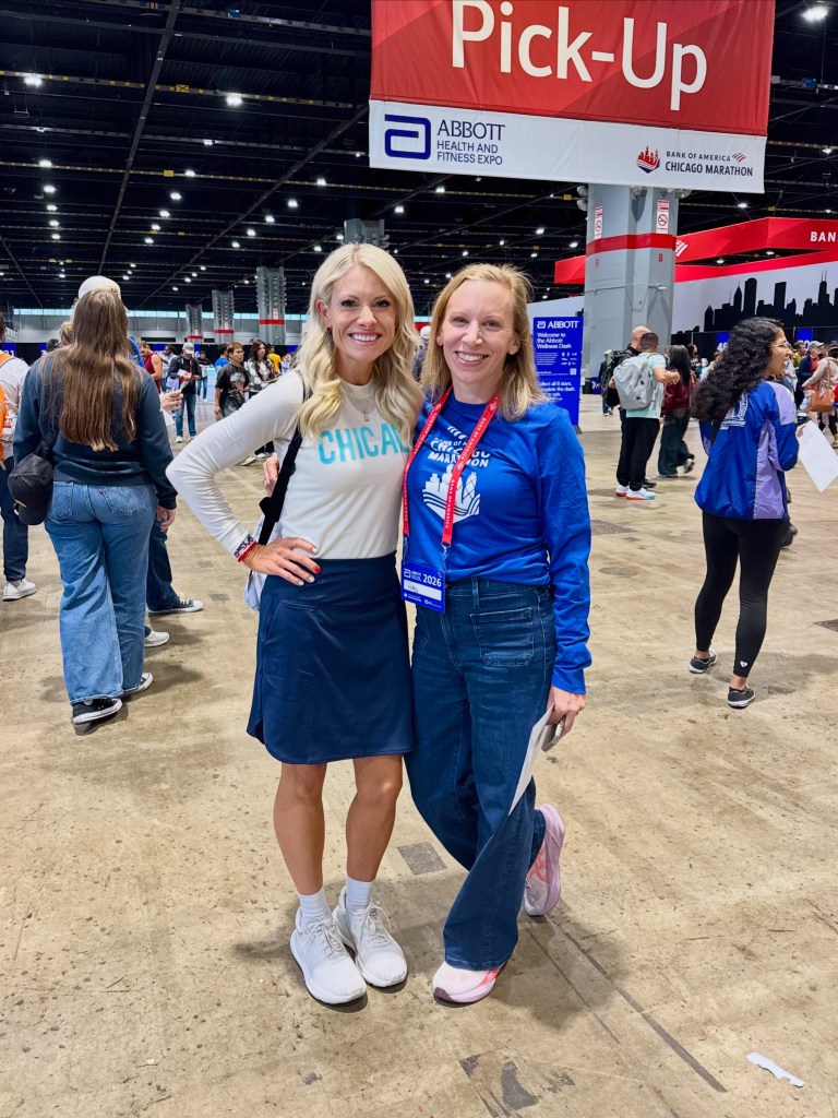 Two women posing for a photo at the Bank of America Chicago Marathon Expo, with a sign indicating 'Pick-Up' in the background.